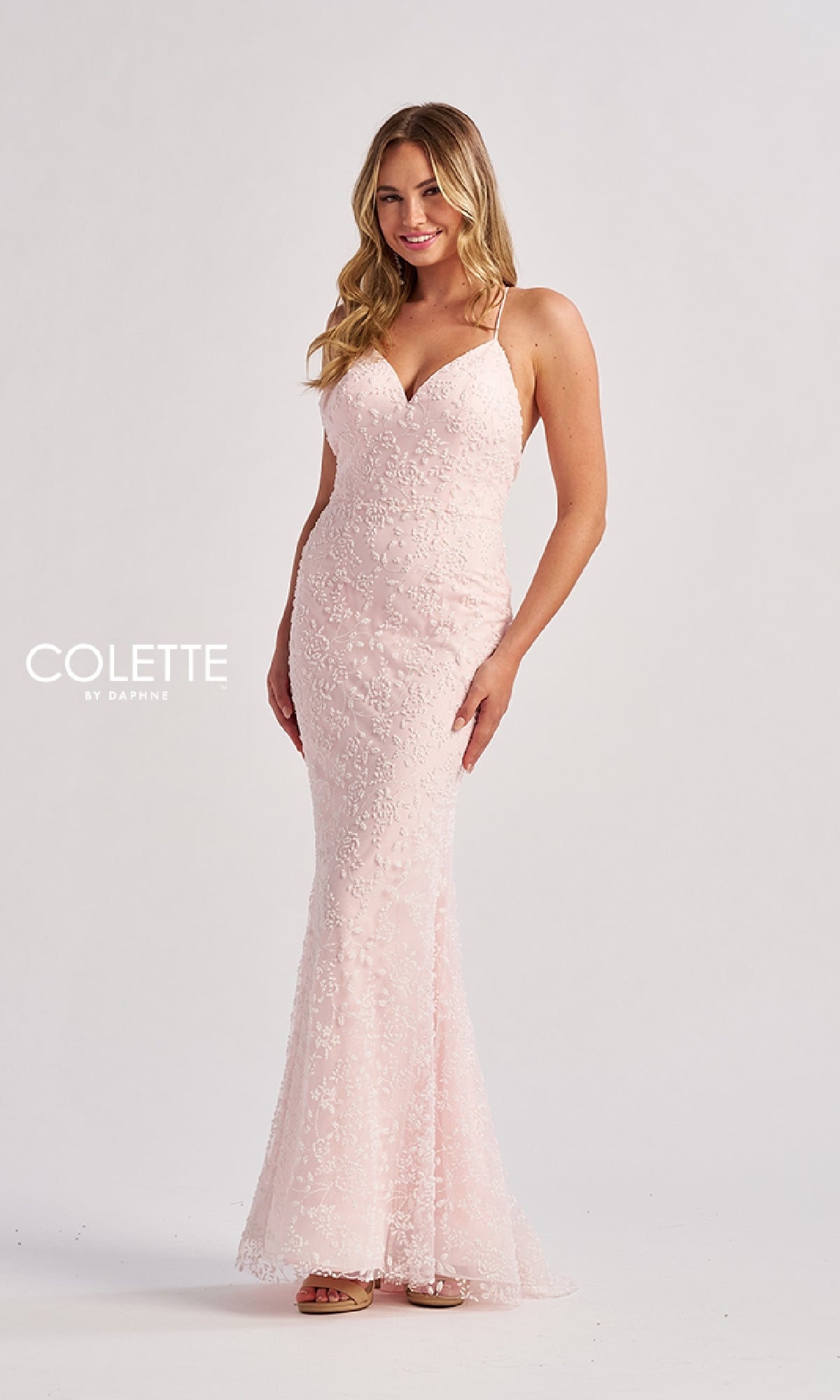A woman poses elegantly against a plain white background, wearing the Colette CL8655 long prom dress—a light pink, floor-length gown with a fitted lace design, delicate spaghetti straps, and a subtle v-neckline.